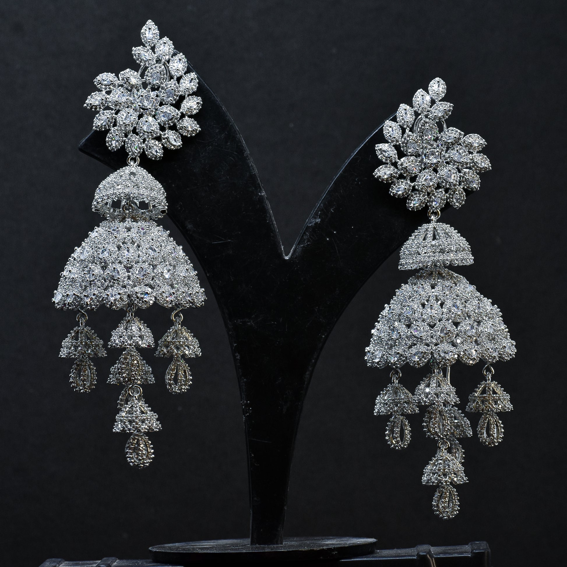 Pair of silver  AD  jhumka earrings on a black stand
