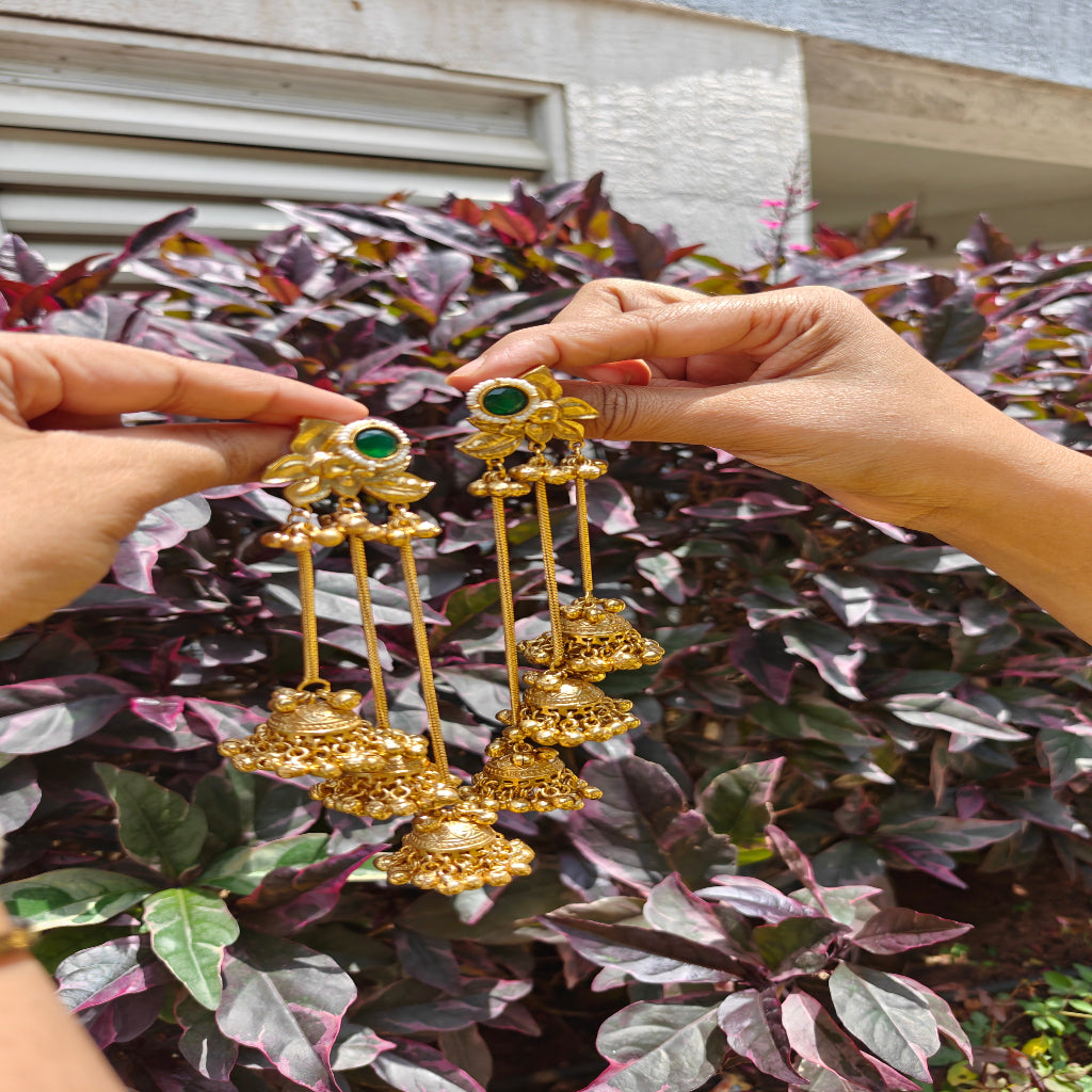 Kahmiri Gold earrings with green gemstones held by hands against a leafy background