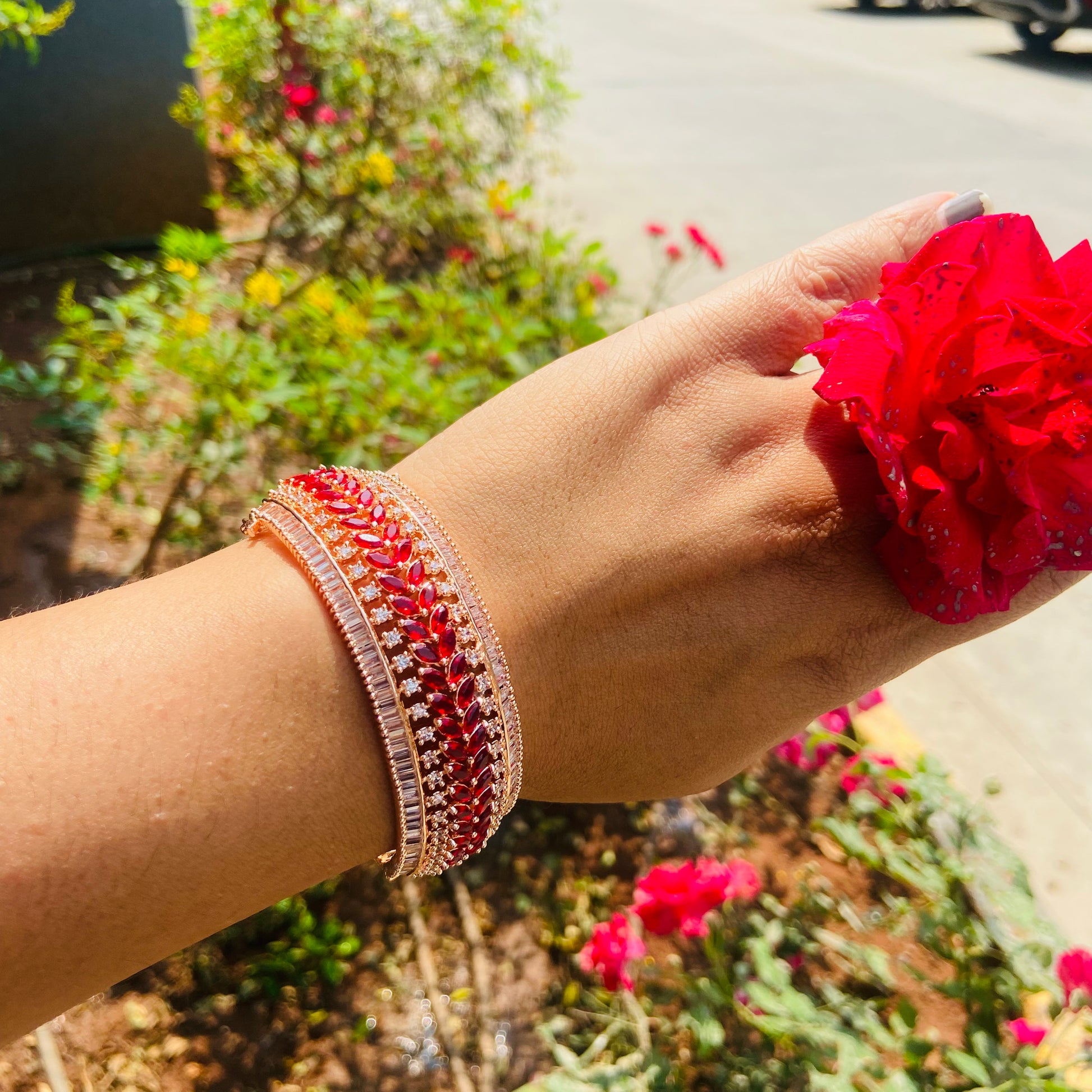 Hand wearing a AD  red beaded bracelet with flowers in the background