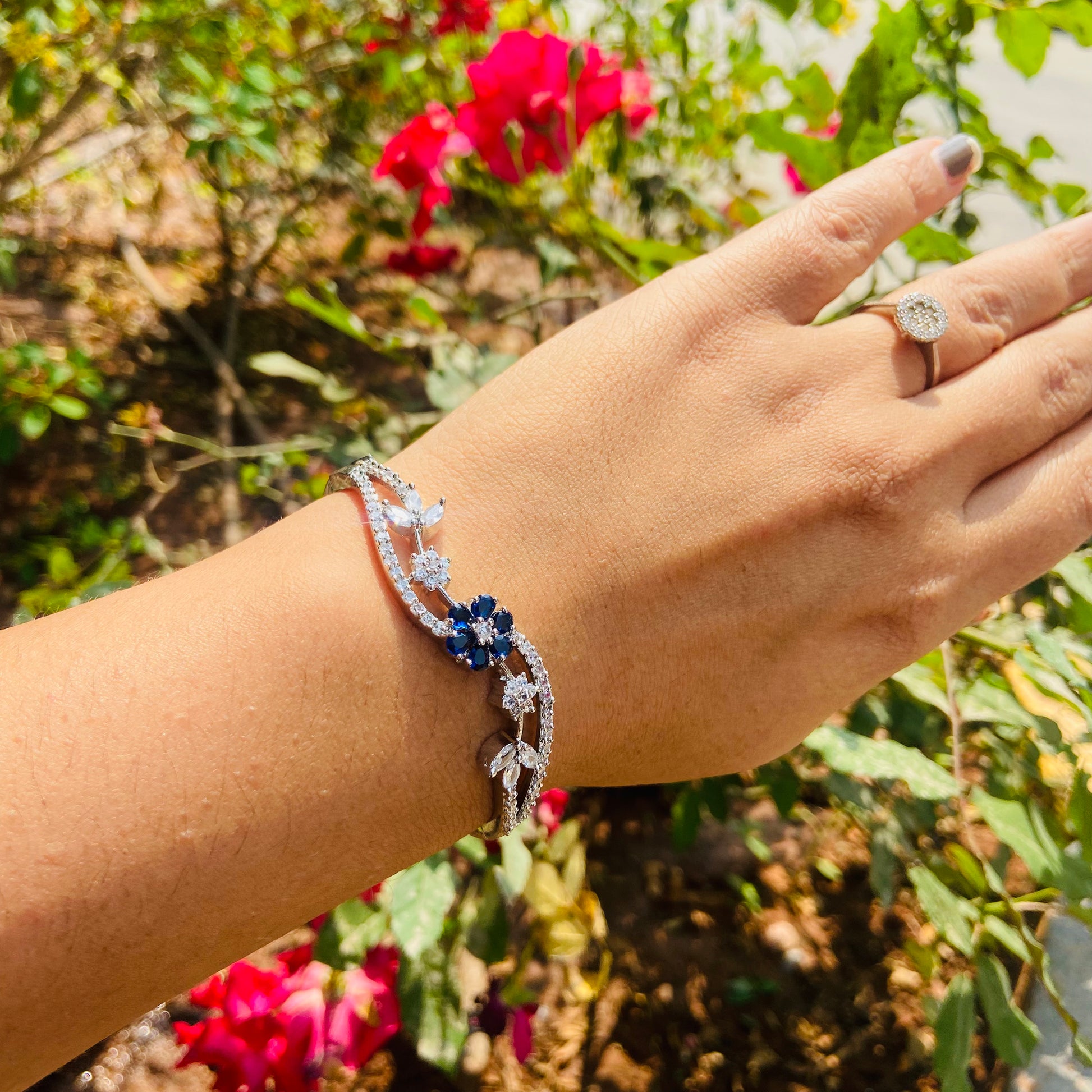 A girl wearing a American Diamond silver bracelet with blue stones against a floral background