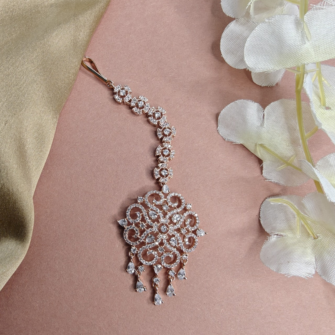 AD Rose gold Mangtikka  with floral design on a pink background with white flowers