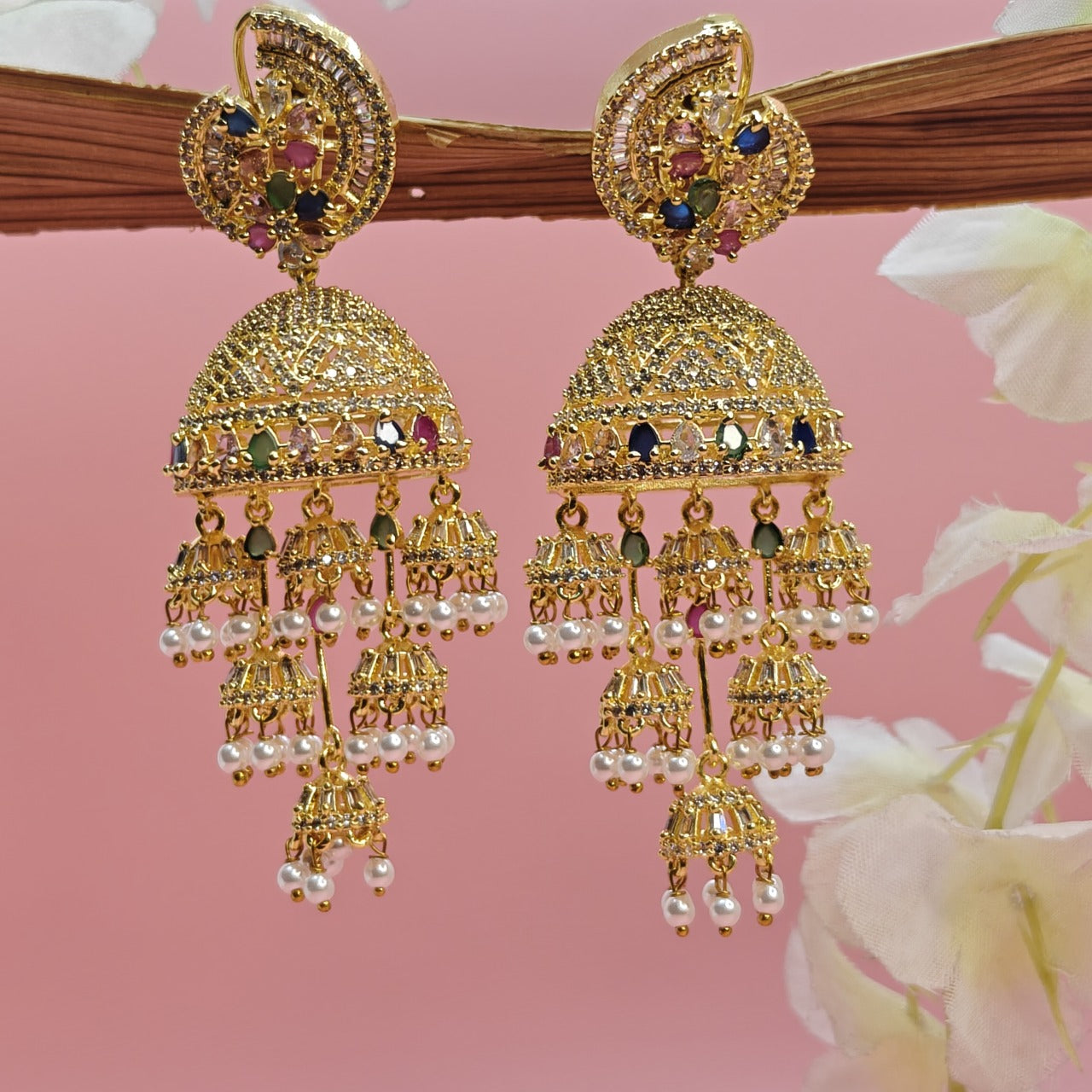 AD Gold earrings Jhumka with colourful AD stones and pearls and gemstones on a pink background