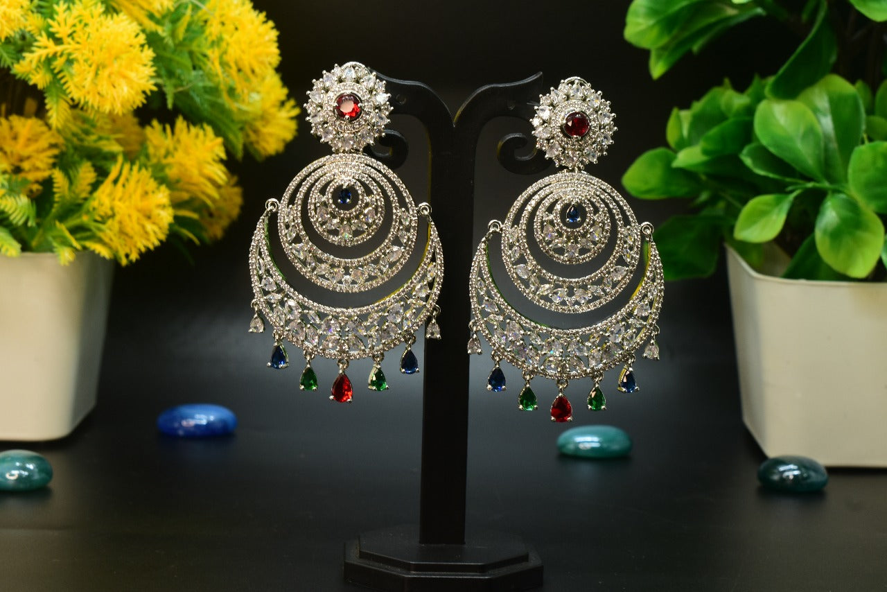 Pair of AD ornate earrings with AD colourful drops on a stand with decorative plants in the background