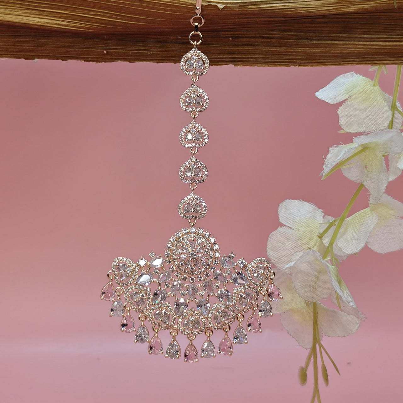 AD Rosegold Mangtikka with AD drops  ornament with crystals on a pink background with flowers