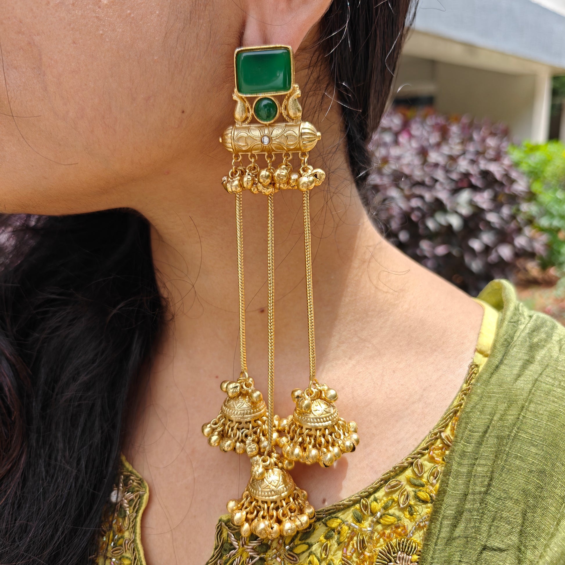 Kashmiri gold earrings with green gemstones worn by a person .
