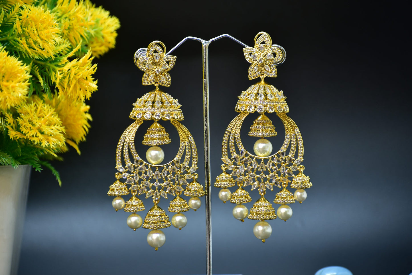 A pair of gold-plated zirconia jhumka earrings displayed on a stand against a black background.