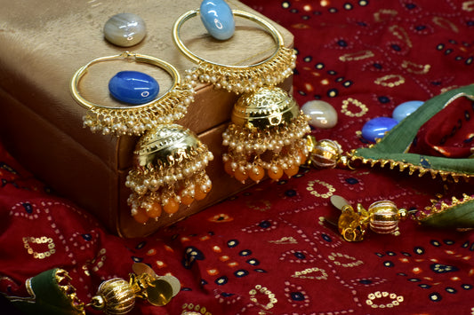 Polki Gold jhumka earrings with orange pearl drops on a red fabric background