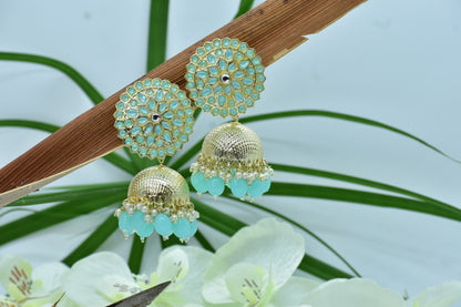 Polki Gold and turquoise earrings on a branch with green leaves and white flowers in the background