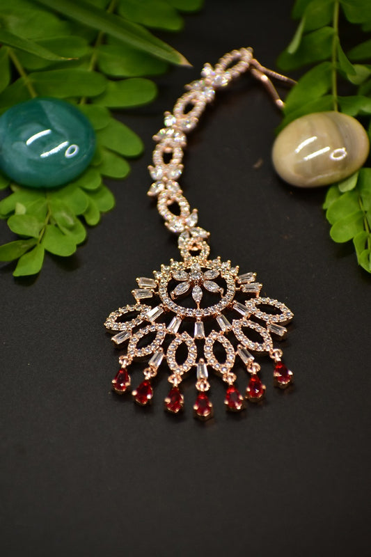AD rosegold Mang tikka with red AD drops displayed on a dark background with green leaves