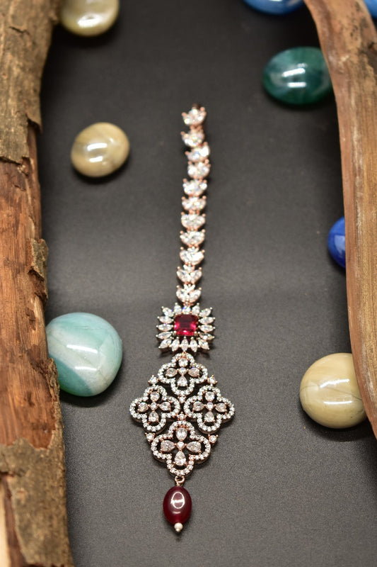 Ad ornate mang tikka with red gemstones and a pearl drop on a black background