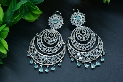 Zirconia Ornate silver Chandbaali earrings with turquoise stones on a dark surface with green leaves.