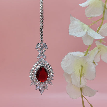 American Diamond Elegant Mangtikka with a red stone and pink background with white flowers.