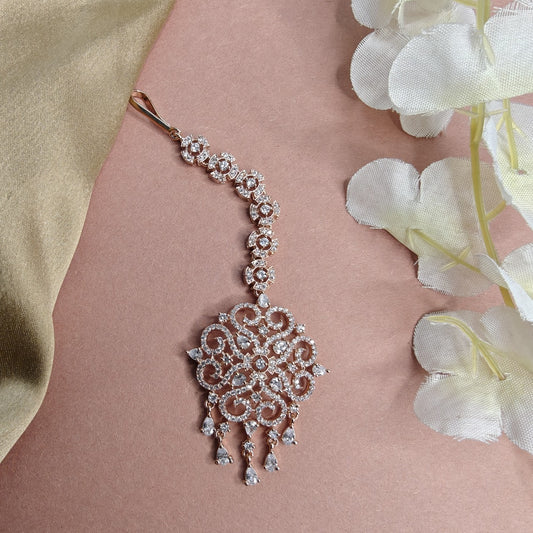 AD Rose gold Mangtikka  with floral design on a pink background with white flowers