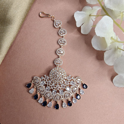 Ornate mangtikka with rose gold and blue accents on a pink fabric background