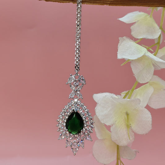 AD Silver polish Mangtikka with a green gemstone on a pink background with white flowershed