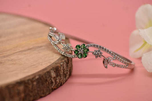 AD Silver bracelet with green gemstones on a wooden block and pink background