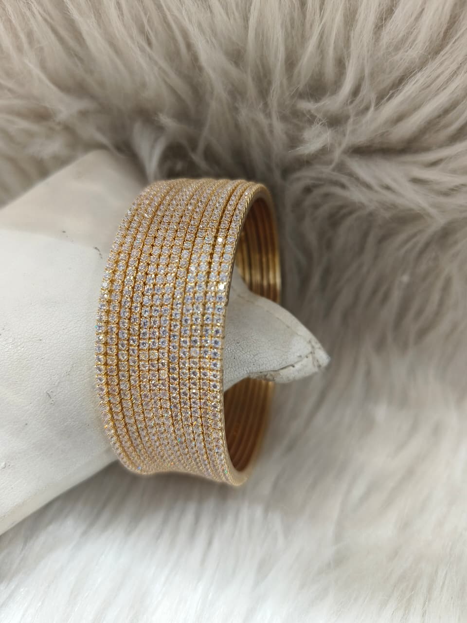 AD Gold bangle with clear stones on a white surface with a fur background