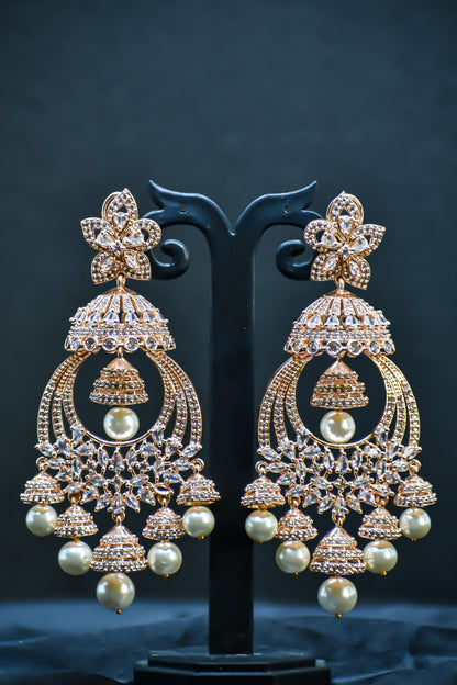 A pair of rose gold-plated zirconia jhumka earrings displayed on a stand against a black background.